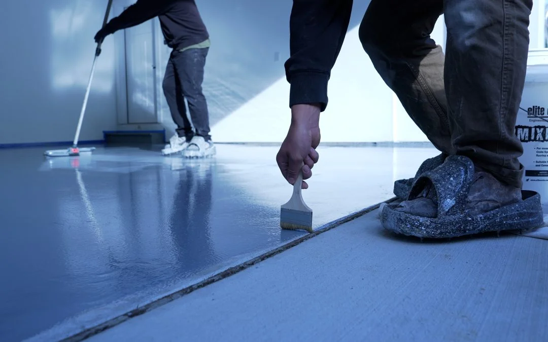 Contractors applying smooth grey epoxy coating to a commercial concrete floor.