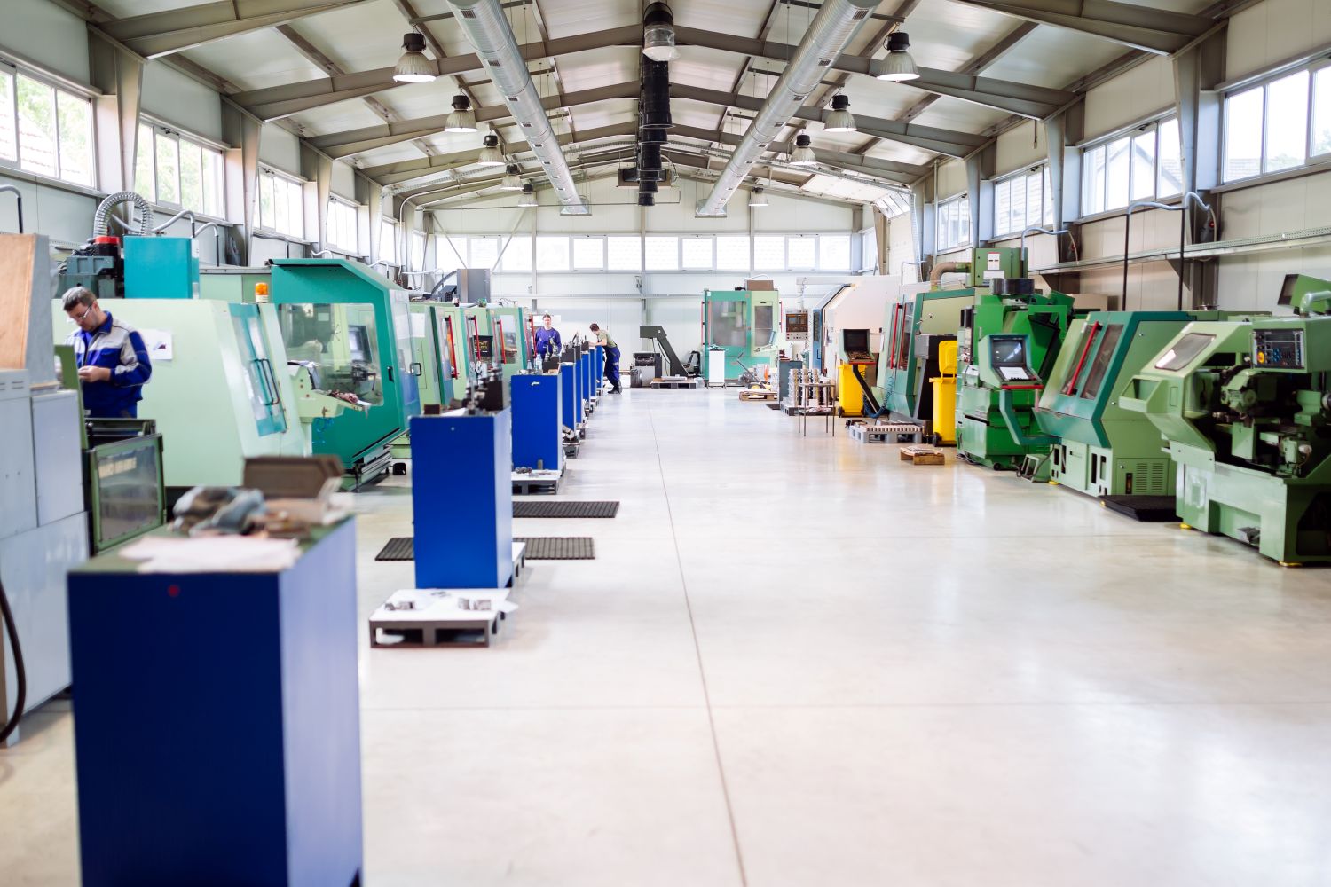 Spacious, clean industrial factory floor with rows of green machinery and smooth concrete flooring.