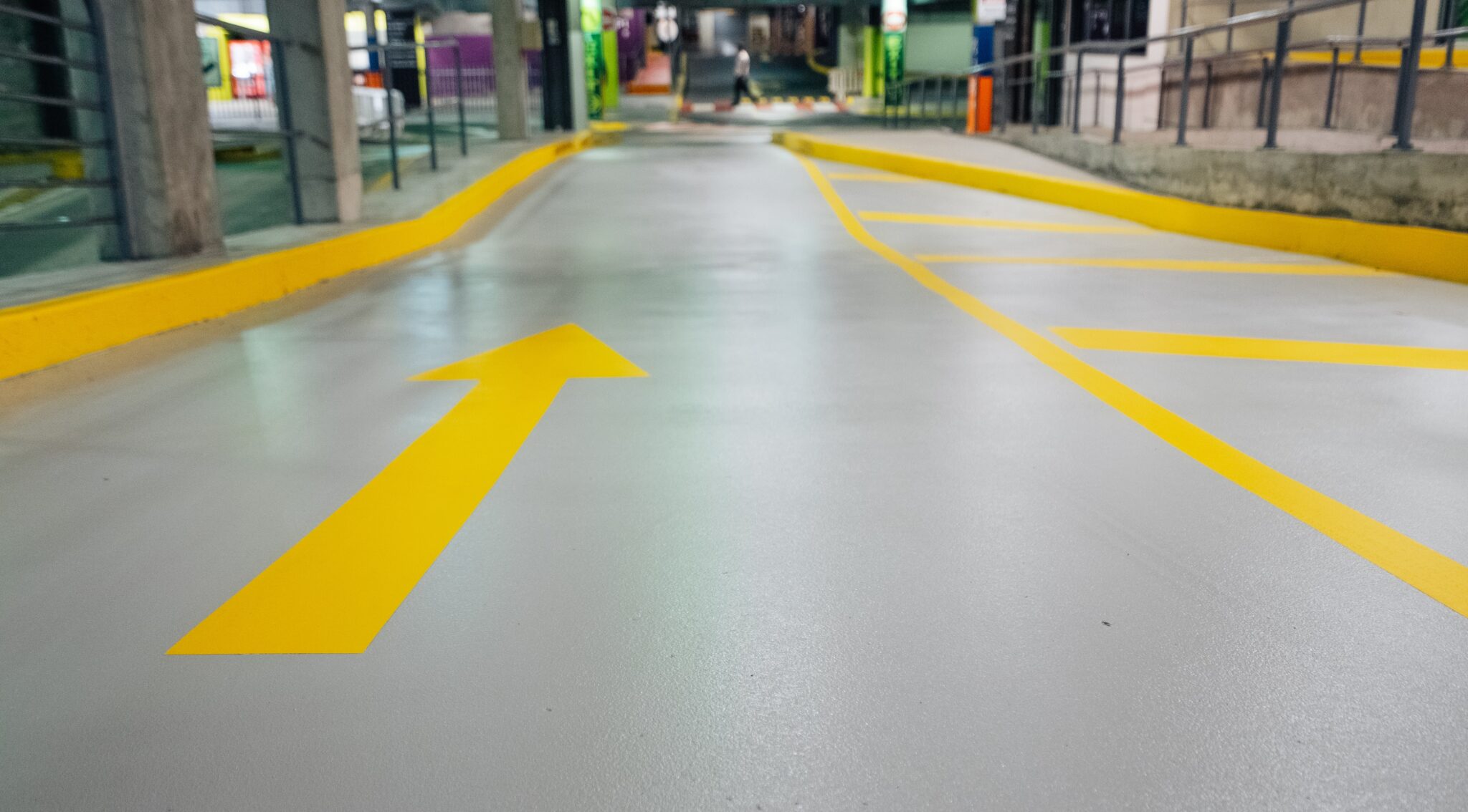 Low-angle view of a smooth grey epoxy carpark floor featuring a bright yellow directional arrow and kerb markings.