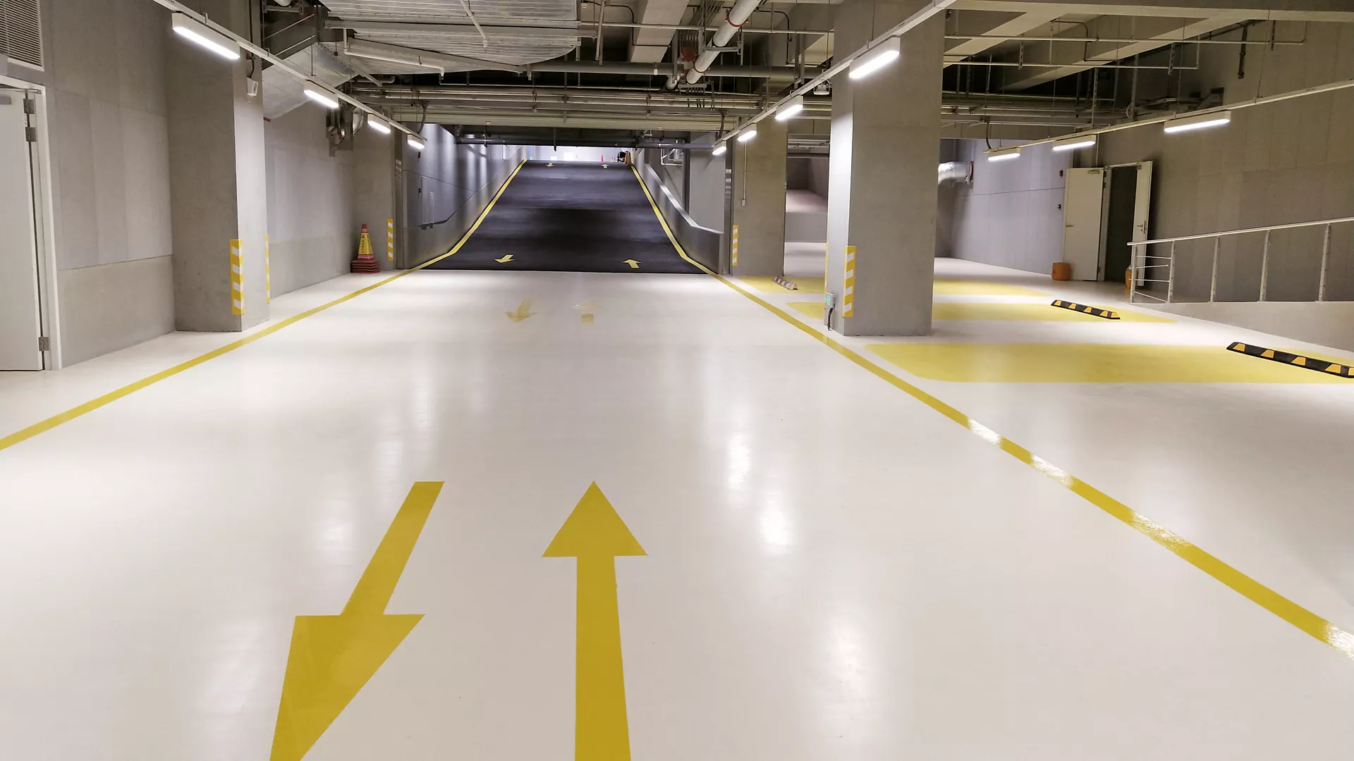 Bright white epoxy carpark floor with yellow directional arrows leading to a dark ramp.