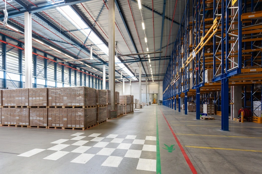 Spacious industrial warehouse interior with durable concrete flooring, pallet racking, and stacks of wrapped stock.