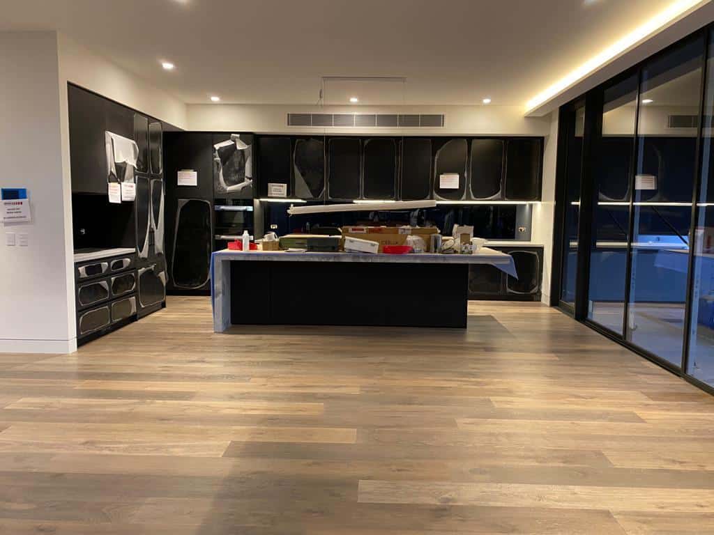 Newly installed light brown timber flooring in a modern kitchen with black cabinets and a large island.
