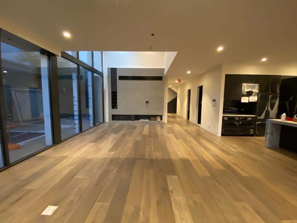 Wide-plank timber flooring installed in a modern open-plan home with large windows and recessed lighting.