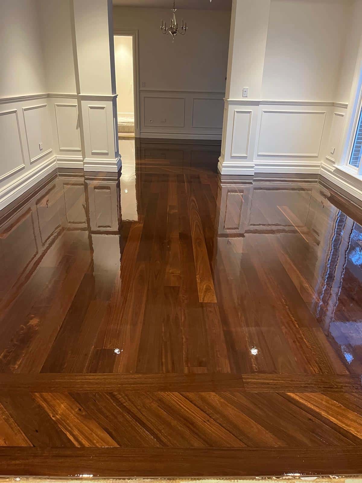Deep brown timber floor with a high-gloss finish reflecting white wainscoted walls.