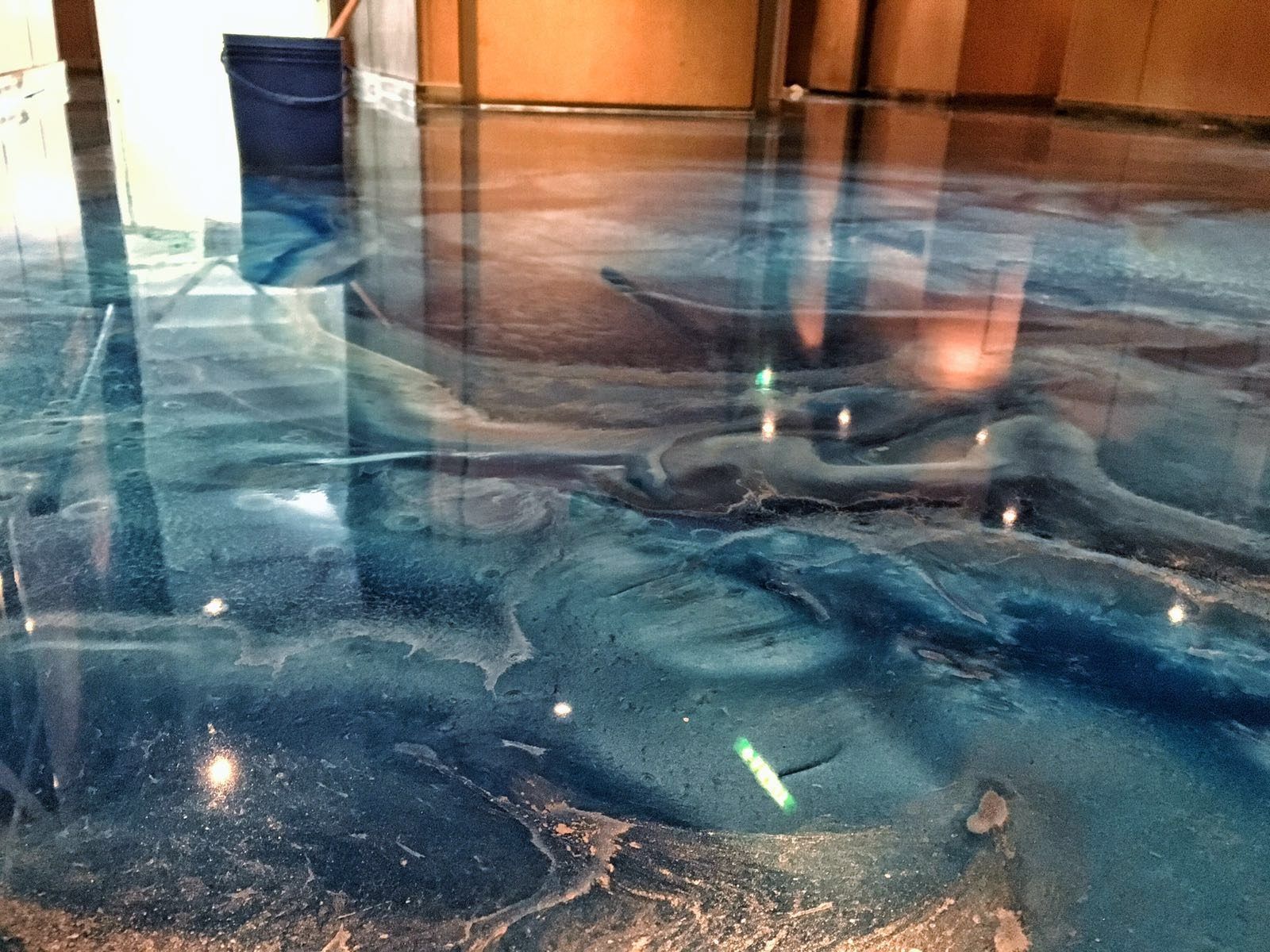 Swirling blue and teal metallic epoxy floor with a high-gloss finish reflecting interior lighting.