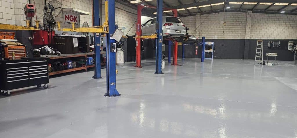 High-gloss grey epoxy flooring in a professional automotive workshop with car lifts and toolboxes.
