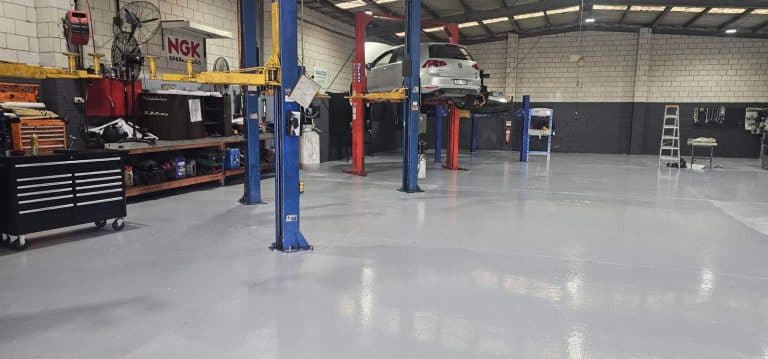 High-gloss grey epoxy flooring in a professional automotive workshop with car lifts and toolboxes.