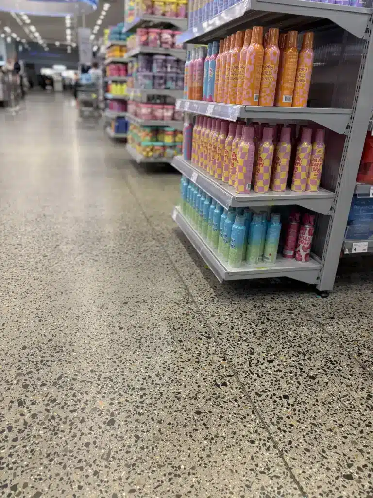 Polished aggregate concrete floor in a retail aisle with colorful product shelves on the right.
