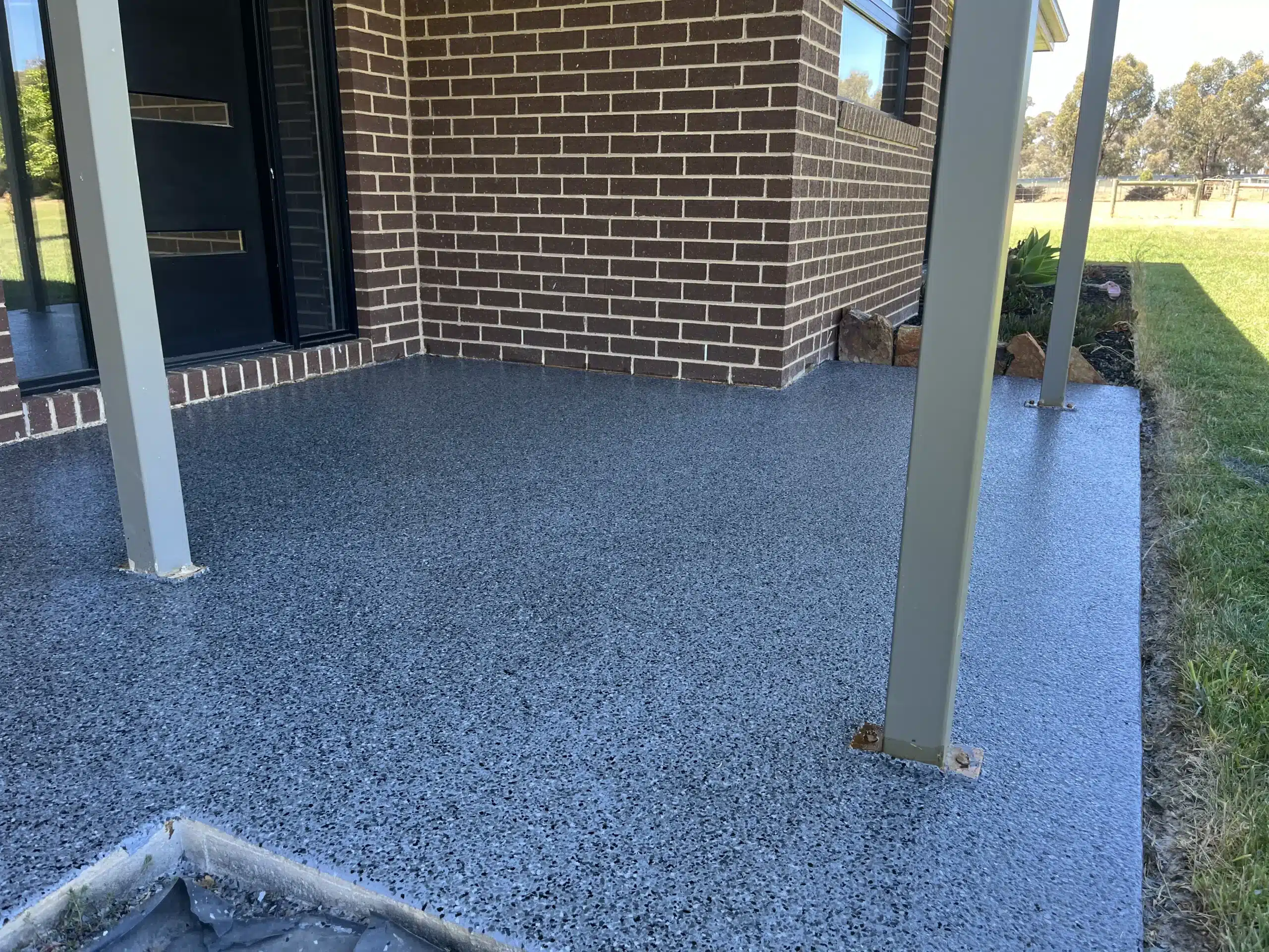 Grey and blue flake epoxy coating on an outdoor residential porch next to a brown brick wall.