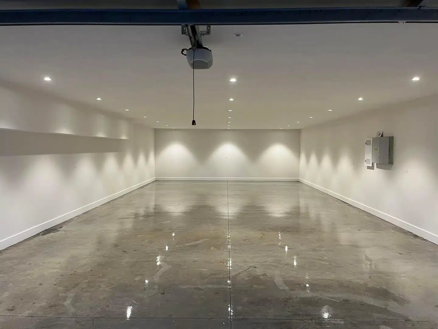 Large empty garage with a reflective grey epoxy floor and warm recessed ceiling lighting.