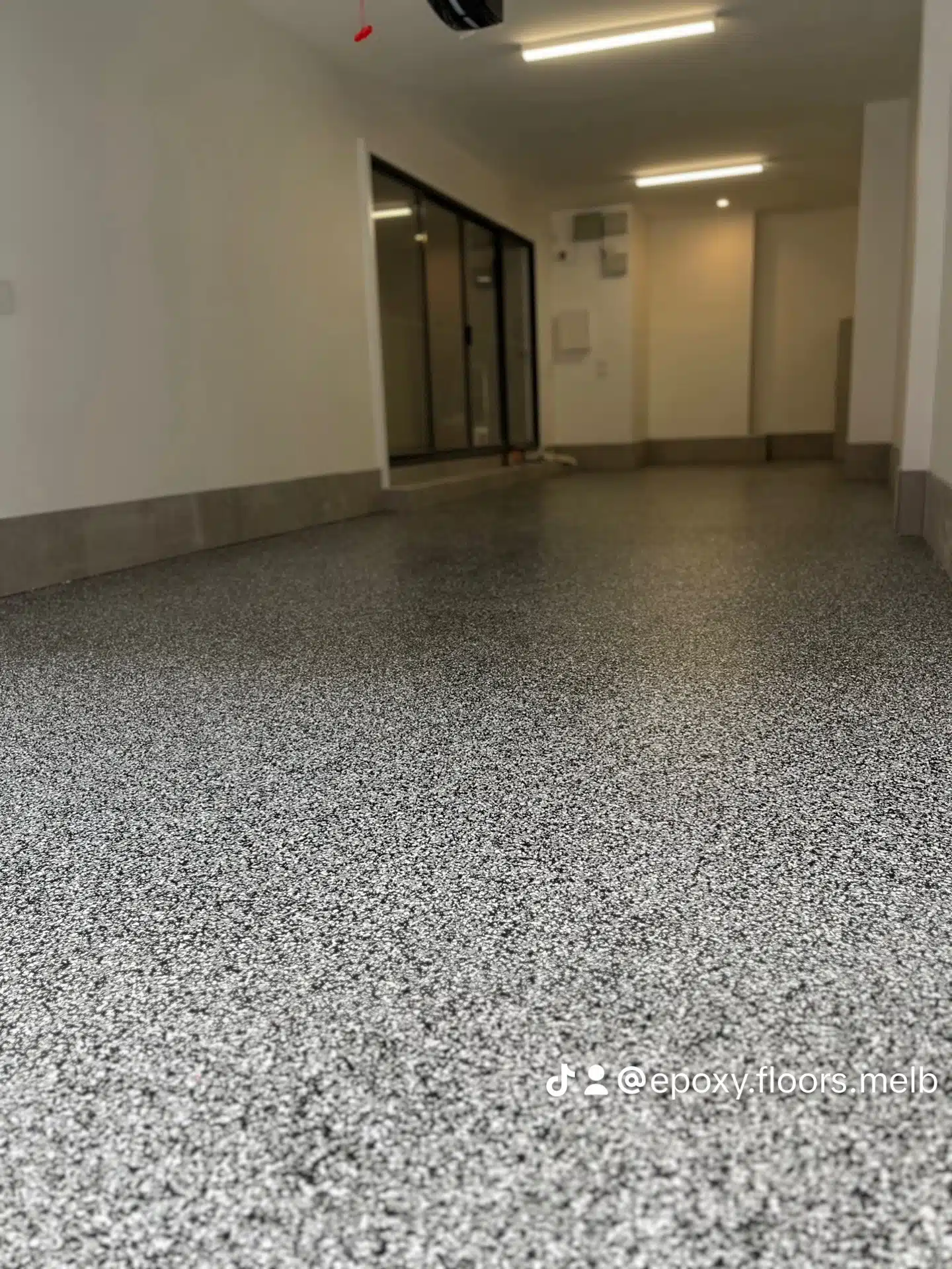 Low angle view of a newly installed grey and white speckled flake epoxy floor in a clean garage.