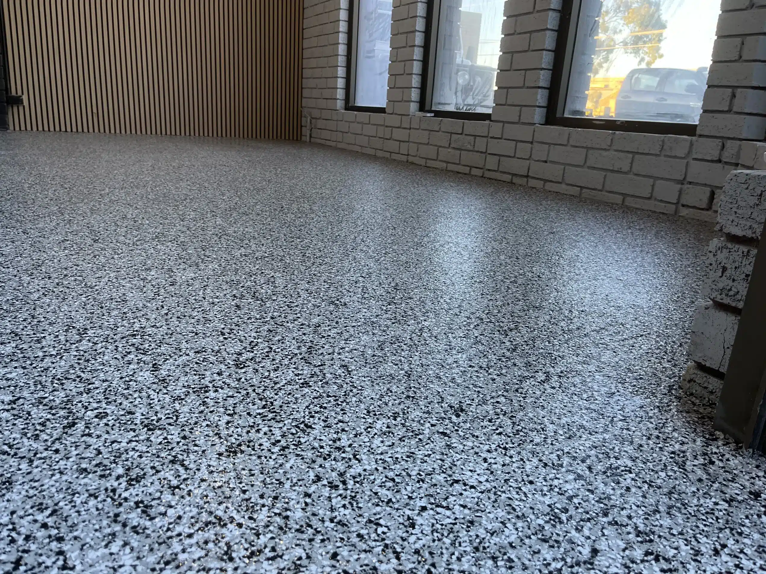 Polished grey and black epoxy flake flooring in a modern room with white brick walls and wood slats.