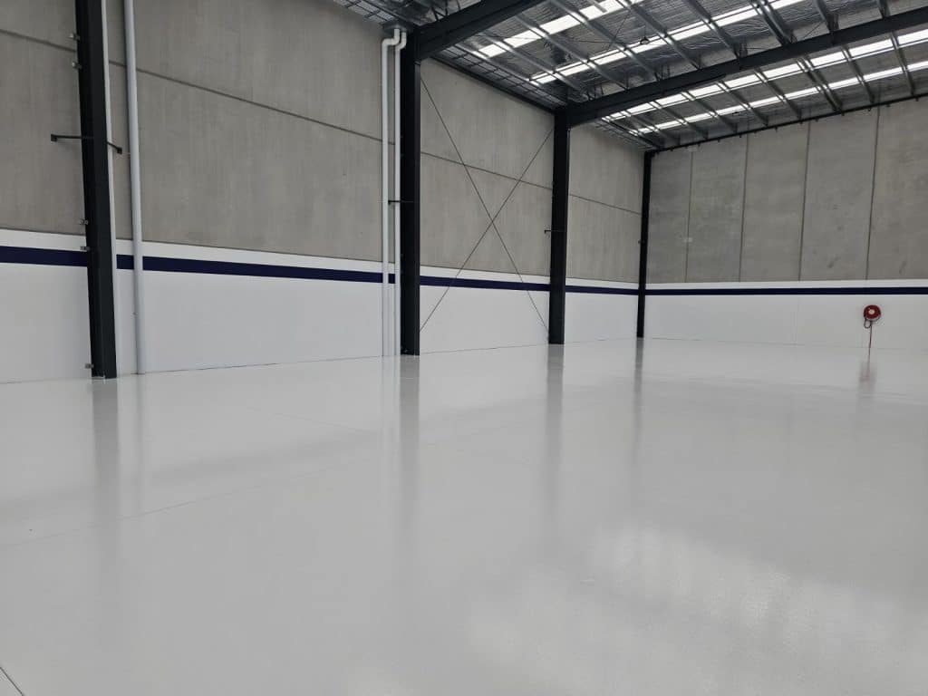 High-gloss white epoxy flooring in a large industrial warehouse with concrete walls and skylights.