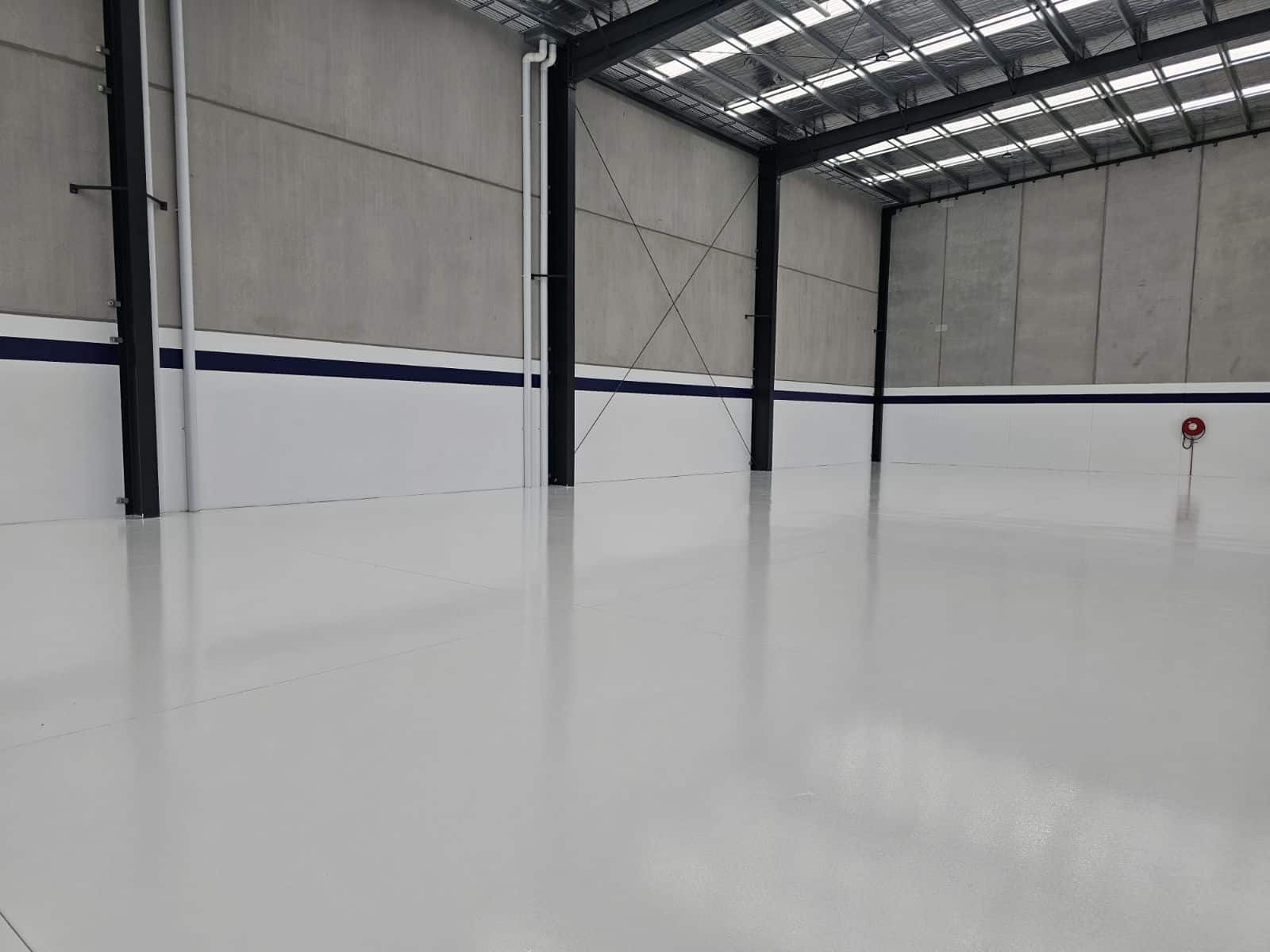 High-gloss white epoxy flooring in a large industrial warehouse with concrete walls and skylights.