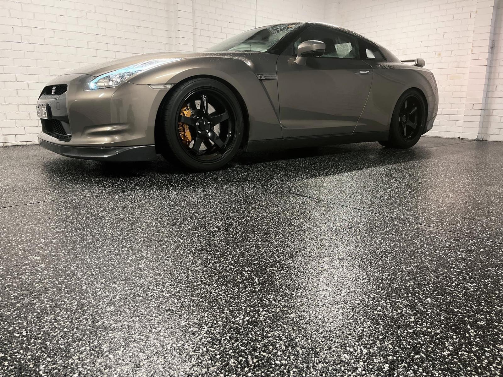 Grey sports car parked on a polished black and white flake epoxy floor in a professional garage.