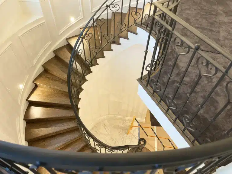 High-angle view of a curved wooden staircase with ornate wrought iron railings during a home renovation.