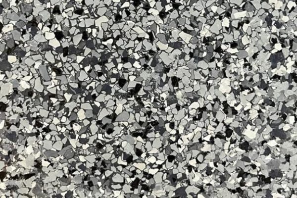 Combat Style Flake Epoxy Flooring Close up of a durable epoxy floor coating featuring a mixture of black, grey, and white decorative flakes.