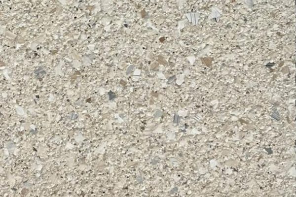 Sandstone Fleck Epoxy Flooring A close-up of a textured epoxy flooring surface featuring a neutral sandstone color with white, gray, and brown flakes.